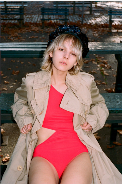 woman sitting on bleacher in red one piece and tan jacket