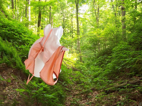 A pink unicorn in the woods with a orange bra and underwear hanging from it.