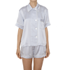 Woman wearing light grey silk collared short-sleeved sleep shirt with left breast pocket and contrast piping and matching shorts