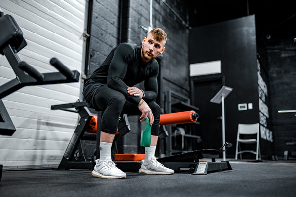 man in black long sleeve shirt and black pants sitting on exercise equipmen in gym