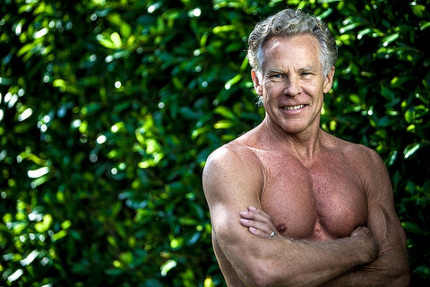a topless man posing in front of bushes