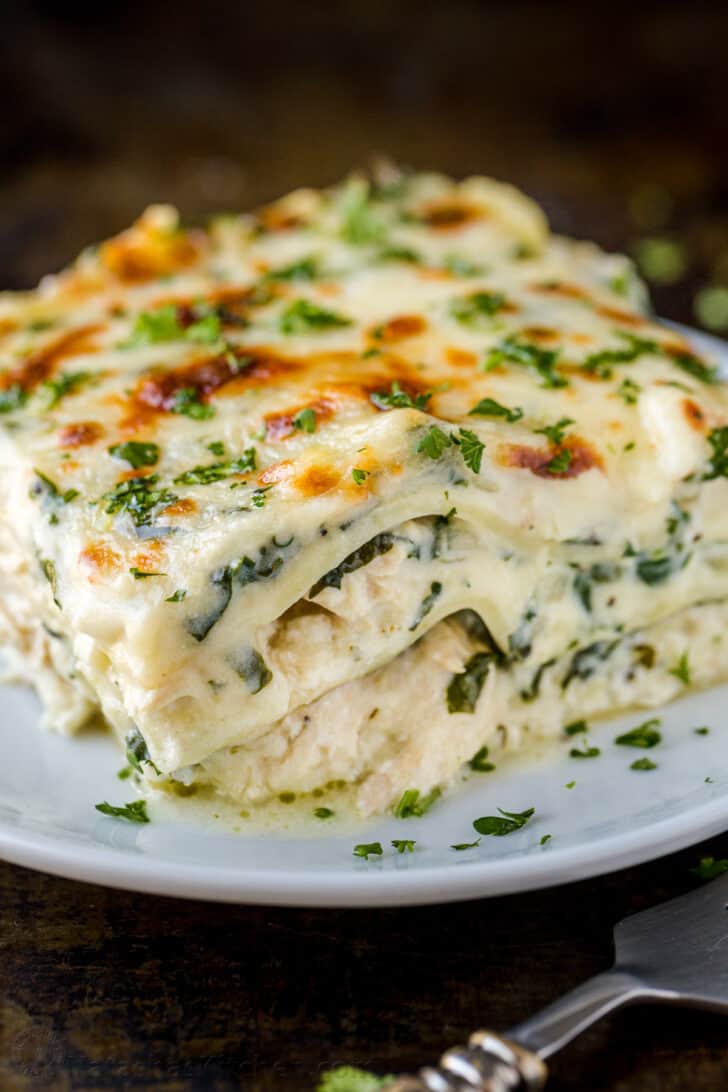 Image of a slice of chicken lasagna on a plate, showing melty cheese and herbs on top. Photo by Natasha Kravchuk.