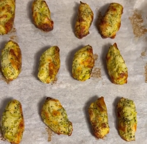 Image of a sheet pan covered in parchment paper with little hand made broccoli tots lined up after baking.