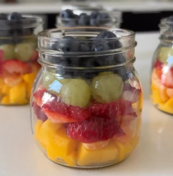 Closeup image of @moribyan's Rainbow Fruit Jars, small palm sized mason jars filled with diced mango, tangerines, strawberries, green grapes, and blueberries. Image from @moribyan on instagram