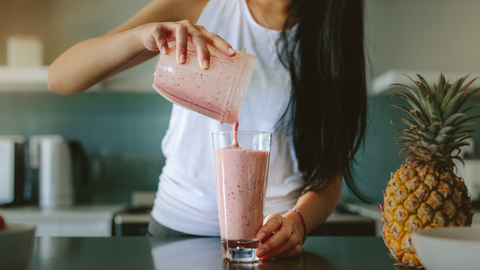 woman pouring smoothie into glass to drink in her kitchen