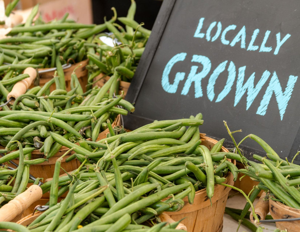 Fresh green beans are piled into straw baskets. A sign reads locally grown.