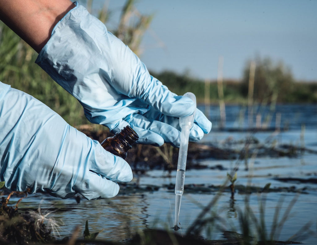 A person wearing latex gloves pulls water into a dropper with one hand while holding a small brown bottle in the other.