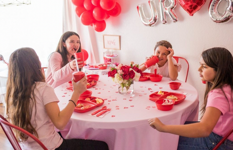 A group of teen girls sitting at a pink table using red re-play cups and bowls