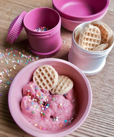 A table with pink re-play products on it.  pink bowl with ice cream and wafter and a pink snack stack with sprinkles