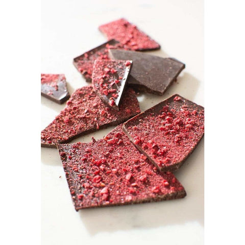 A block of Kakadu Plum Co Pepperberry and Raspberry Dark Chocolate broken into smaller pieces. Dark chocolate with beautiful red dried berries scattered over the top.