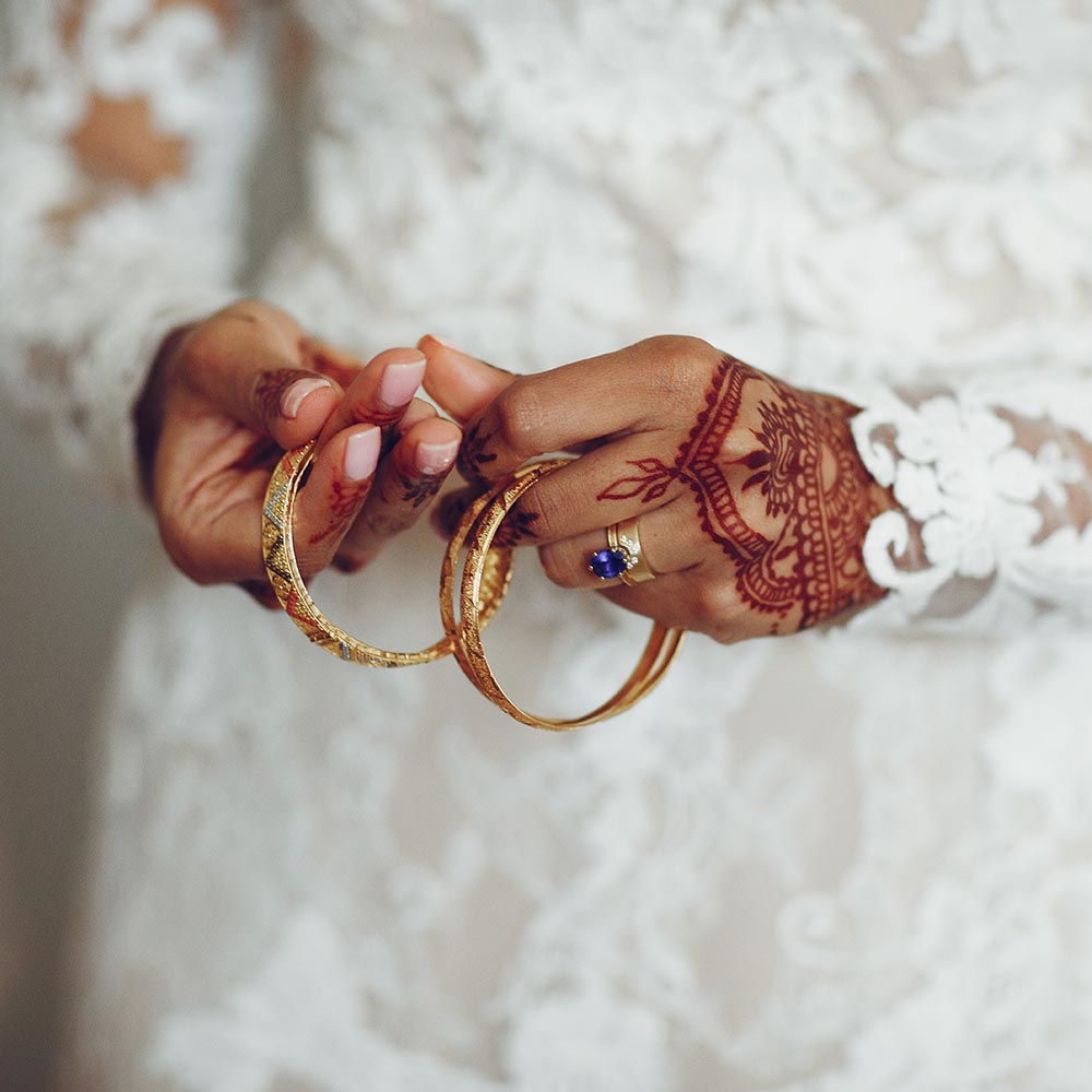Bride holding gold bangles with full sleeved lace wedding dress