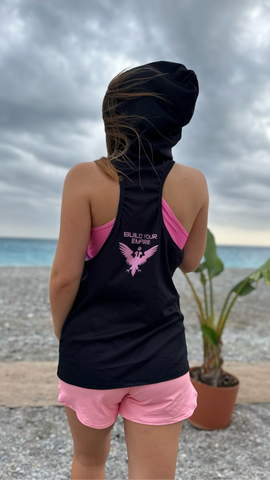 Czarina Sasha (@sashastarynets) wearing a black and pink sleeveless Build Your Empire hoodie and pink shorts from Czar Clothing on the beach in Nice, France.