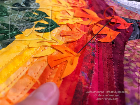 Breakthrough fabric art process picture, with hand pushing an embroidery needle through a brightly colored bird to make an arrow shape.