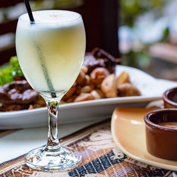Pisco Sour Cocktail auf einem Tisch mit Essen im Hintergrund