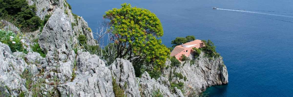 Villa Malaparte a Capri, denominata anche "Casa come me", costruita su un costone di roccia nei pressi dei Faraglioni a Capri, nella baia di Marina Piccola. In primo piano un grande pino marittimo e sullo sfondo il mare azzurro di Capri