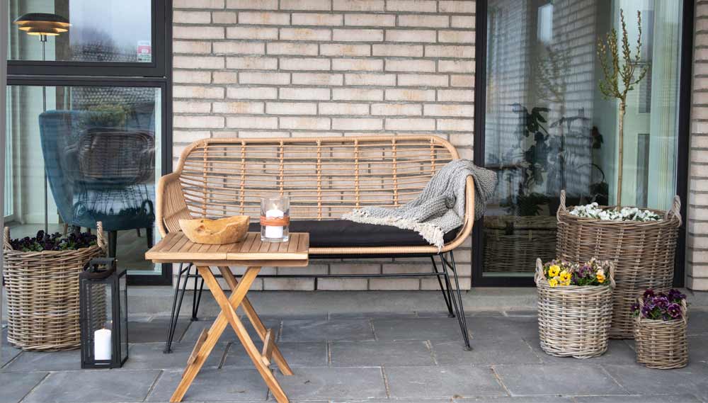 A Loft&Vintage webshop skandináv, nordic stílusú kollekciójának hangulatképe, fém és rattan kanapé egy modern téglaház teraszán natúr kiegészítőkkel, fa kisasztallal.