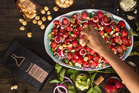 Watermelon and Feta Salad Topped with Rosé Popcorn with hand putting more popcorn