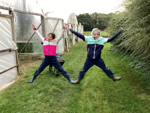 Two children jump in the air outside polytunnels