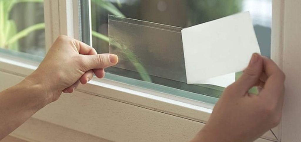 Hands applying the clear fly glue trap on window.