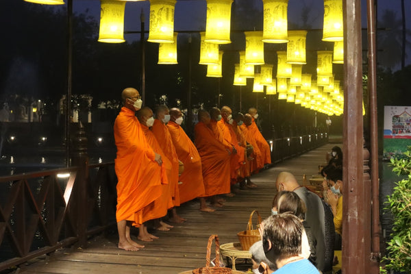 Mönche in einer Reihe auf einer Brücke vor den Gläubigen, die nach den Spendengaben einen Segen singen