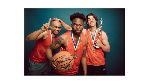 3 Men Wearing an Orange Jersey. Each of Them has a Medal One is Holding a Trophy and the other a Basketball ball.