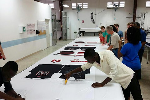 A team examines and prepares to cut newly sublimated jerseys in a factory in front of a group of people