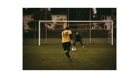 A Guy Wearing a Yellow Jersey is About to Kick The Soccer Ball Towards The Goal.