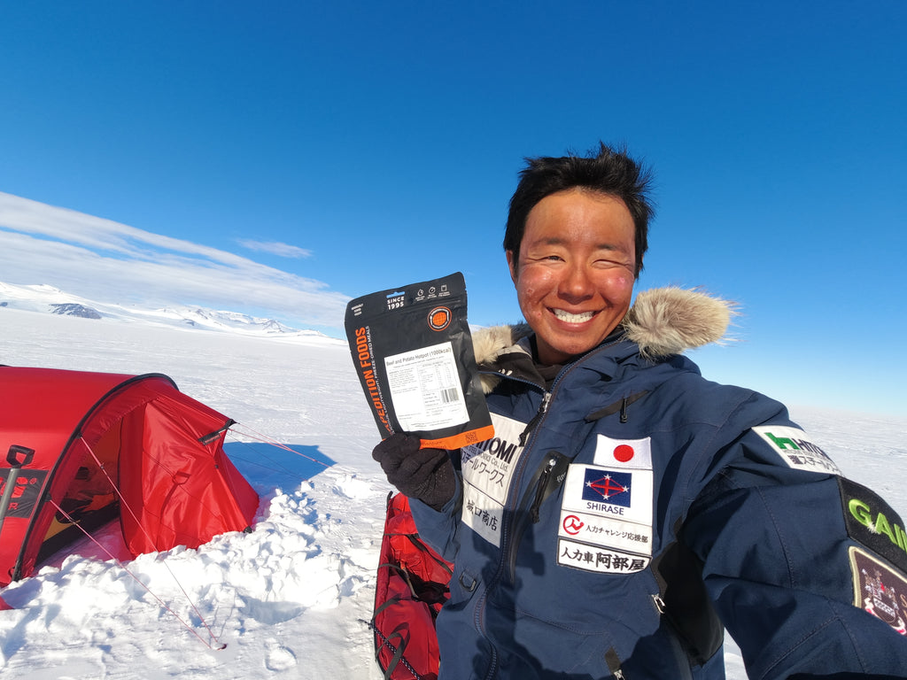 A person holding a meal pouch in front of a tent.