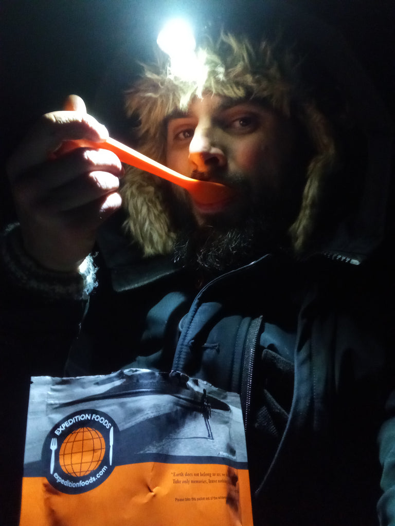 A mn in very warm winter gear eating an Expedition Foods freeze-dried meal.