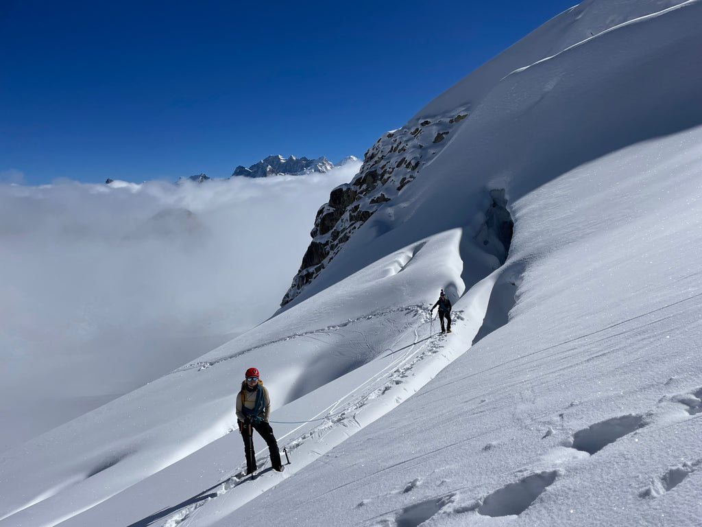 climber standing on snow slope with mountains and blue skies in background