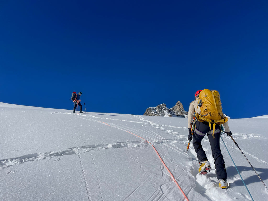 Climber walking up a snow slope towards another roped up climber