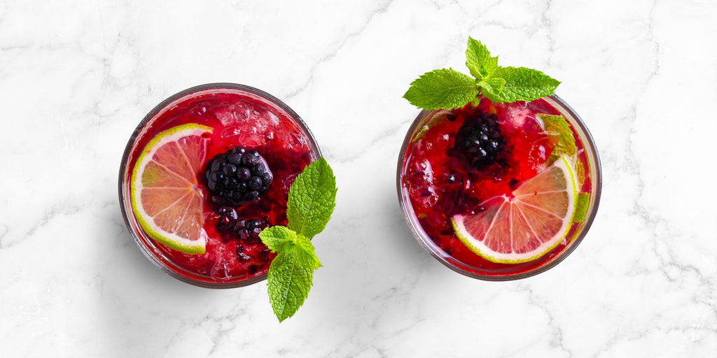 An overhead image of two ZOKU Blackberry Mojitos on a light stone surface.