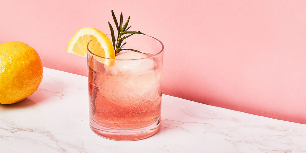 An image of ZOKU’s Rosemary Pomegranate Cocktail against a pink background.