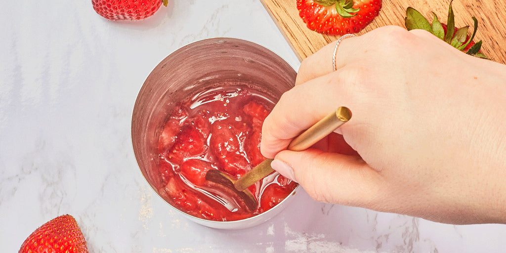 An image of a hand muddling strawberries in a cocktail shaker.