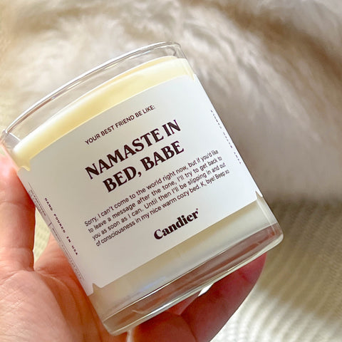 a glass candle with a label that reads Namaste In Bed Babe