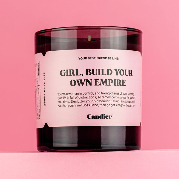 A black glass candle with a pink label that reads Girl Build Your Own Empire