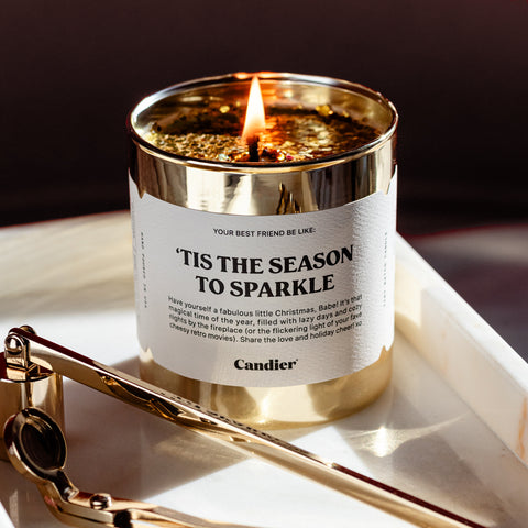 A gold Christmas themed scented candle with a label that reads 'Tis The Season To Sparkle