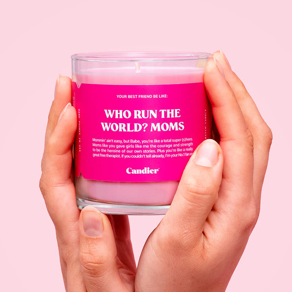 Hands holding a pink candle with a label that reads Who Run The World? Moms