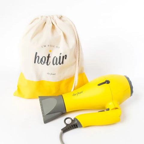 A bright yellow travel hair dryer beside a canvas bag that reads Hot Air