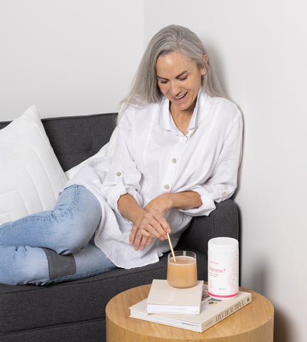 Woman sitting on the couch in her morning routine taking beauty and gut health supplements.