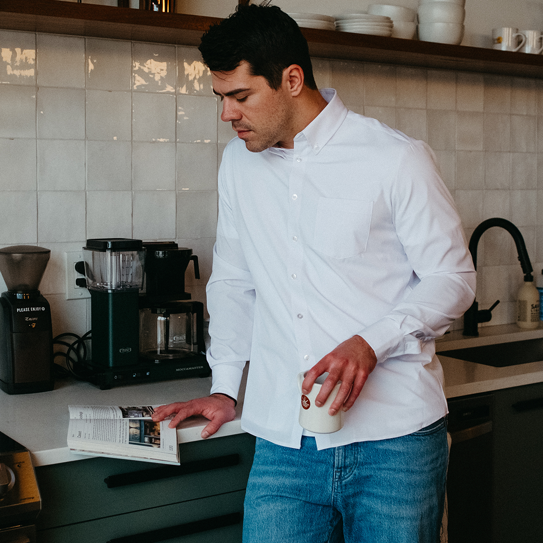 Man in white shirt reading a book in a kitchen.