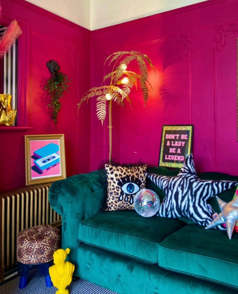 living room with bright pink walls a green velvet sofa and lots of leopard print