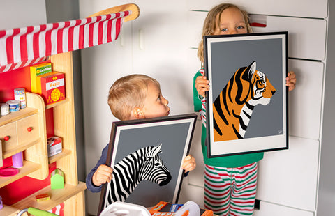 Kids bedroom image with two young boys holding framed prints of a tiger and zebra