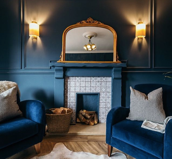 Stunning blue living room showing a fireplace with tiles and blue surround, blue walls with glowing lights and 2 blue velvet armchairs