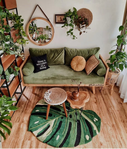gorgeous living toom with wooden floors, green velvet sofa and abundance of plants on the walls and shelves