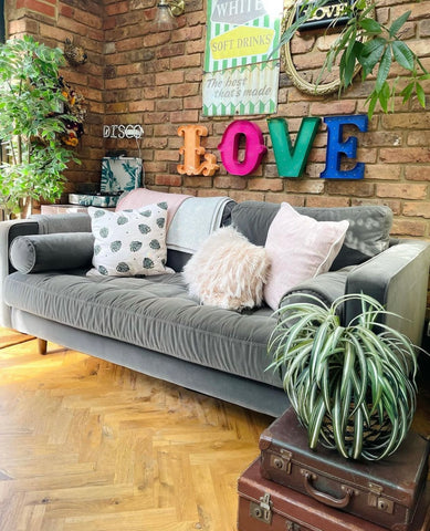 funky living room with grey sofa and large bold letters spelling love over it. lots of plants and cream cushions