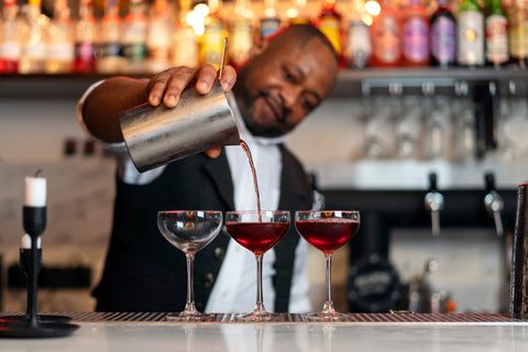 Bartender pouring red cocktails into martini glasses at a bar counter