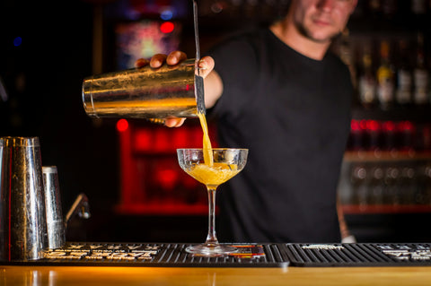 Bartender pouring cocktail into martini glass at bar counter with blurred background