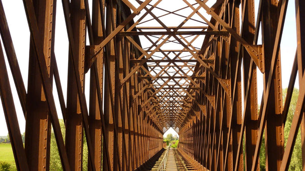 Corten steel bridge with rusted finish and sleek design, supported by slender beams and cables.