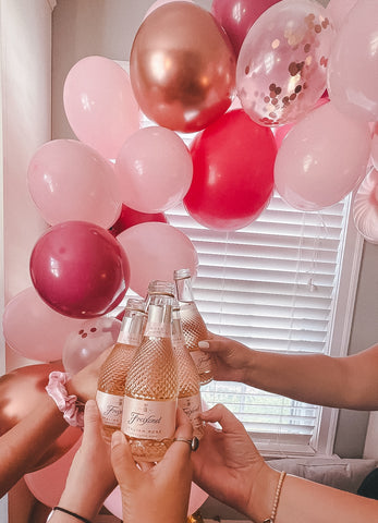 Pink balloons and girls holding small rose bottles 